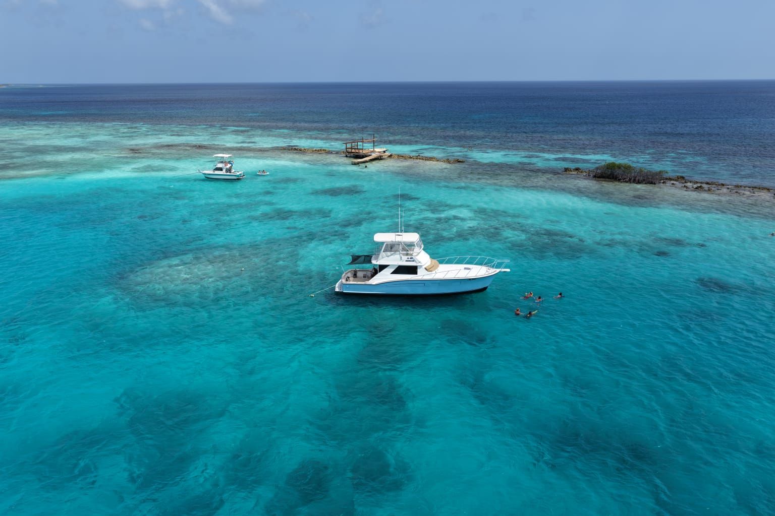 Cocolizo anchored over a turquoise reef in Aruba with guests swimming alongside